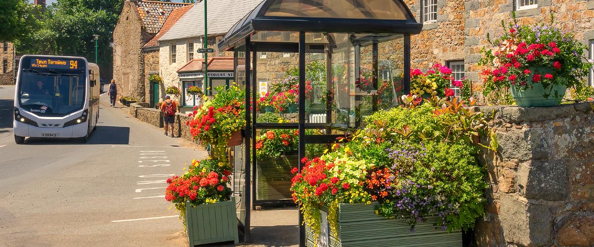 Bus driving past flowers in front of Forest Stores, Guernsey