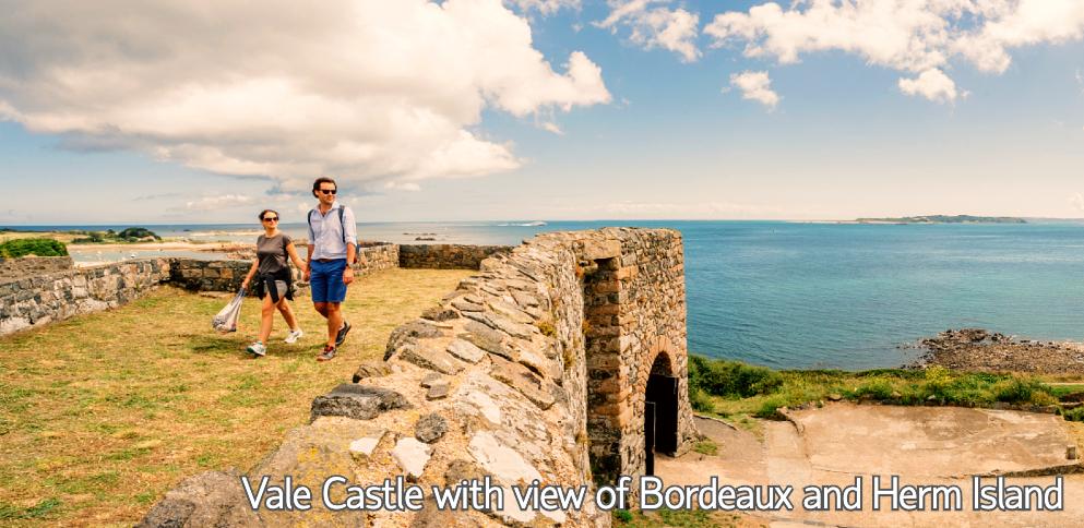 Couple walking on Vale castle with view of Bordeaux and Herm Island in background