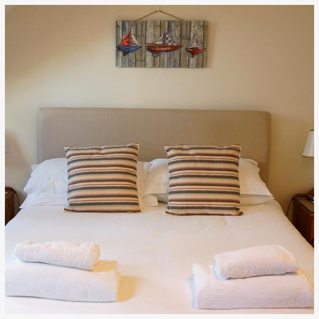 bed with cushions and towels at The Ellingham Cottages, St Martins, Guernsey